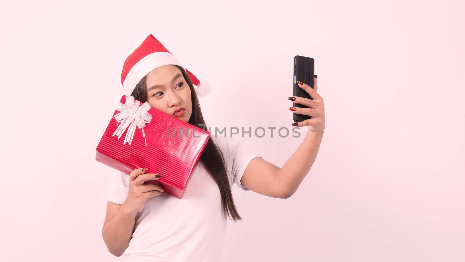 Girl hold gift box make selfie or video online with x-mas christmas prop decoration. Asian Thai teen woman taking online-selfie to celebrate festive season with her friend by red giftbox. studio shot.