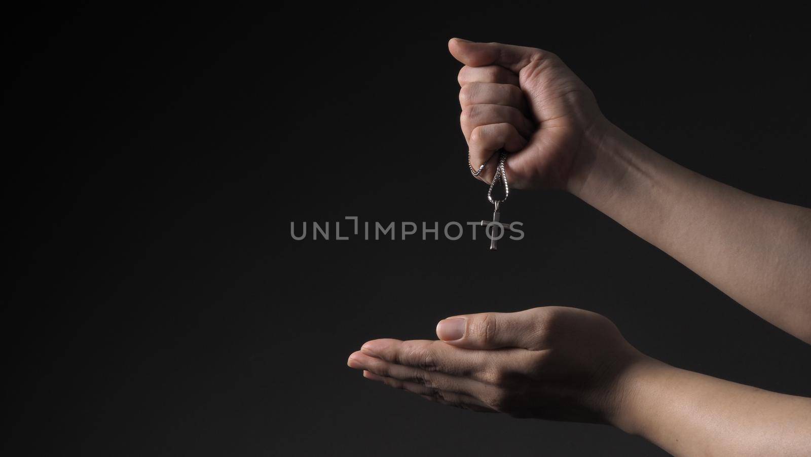 Cross or crucifix pendant and necklace in man hand on black color background in studio which represent praying for god or jesus and thank gods for giving peaceful and faithful to people. silver cross. religion belief concept.