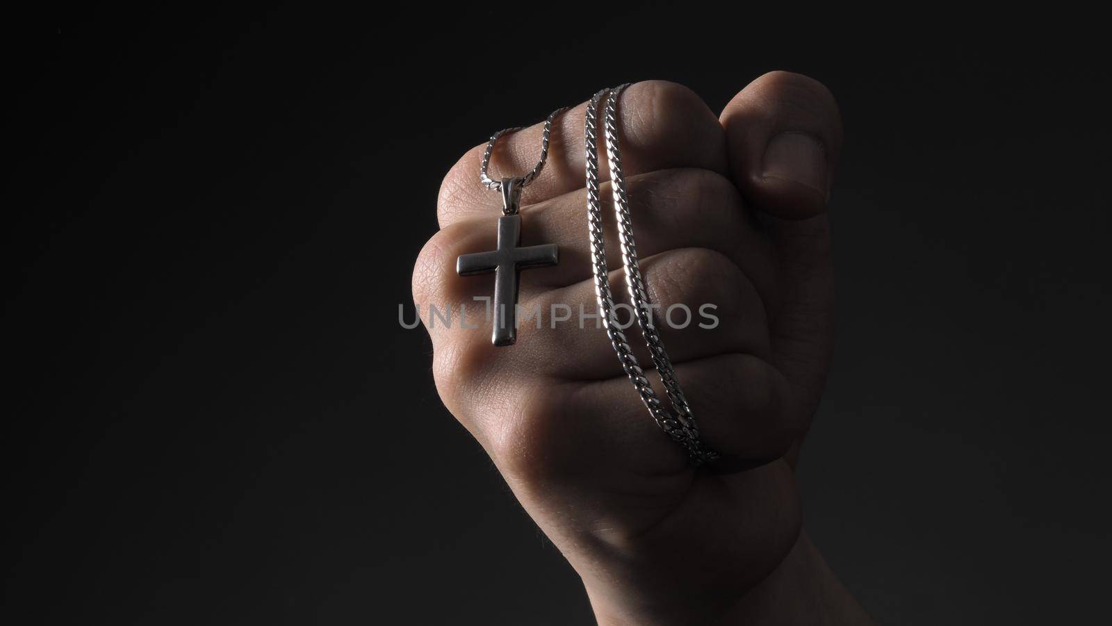 Cross or crucifix pendant and necklace in man hand on black color background in studio which represent praying for god or jesus and thank gods for giving peaceful and faithful to people. silver cross. religion belief concept.