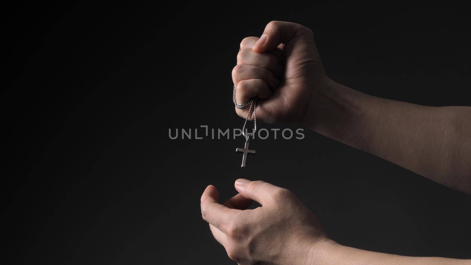 Cross or crucifix pendant and necklace in man hand on black color background in studio which represent praying for god or jesus and thank gods for giving peaceful and faithful to people. silver cross. religion belief concept.