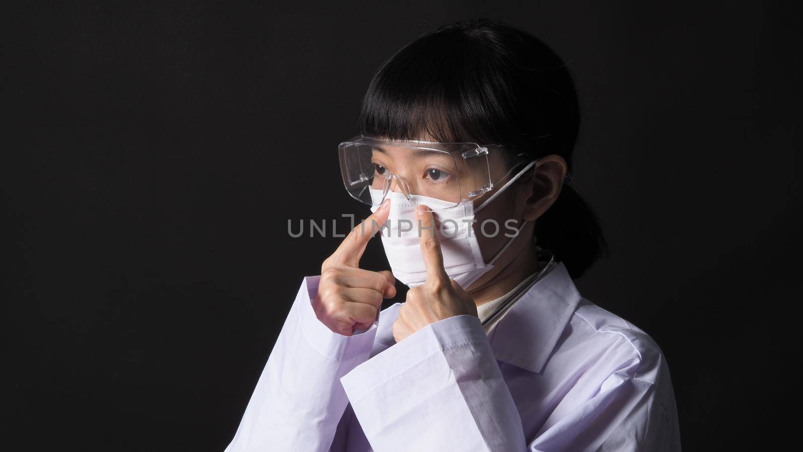 Doctor Wearing Medical Mask and clear goggles or glasses and stethoscope on the neck and white uniform. Asian female doctor or scientist in protective facial masks on black background. protect Covid 19 concept.
 

