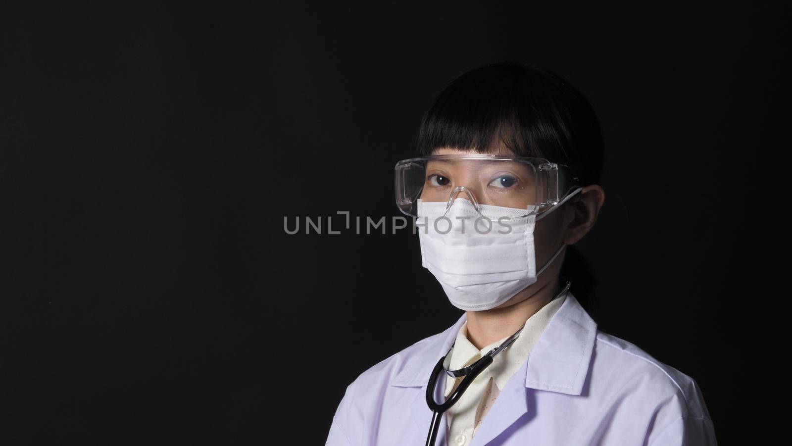 Doctor Wearing Medical Mask and clear goggles or glasses and stethoscope on the neck and white uniform. Asian female doctor or scientist in protective facial masks on black background. protect Covid 19 concept.
 
