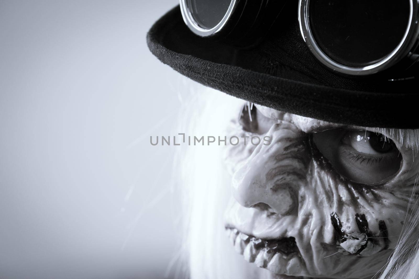 Woman with monster face and black hat wearing steampunk glasses. White hair.