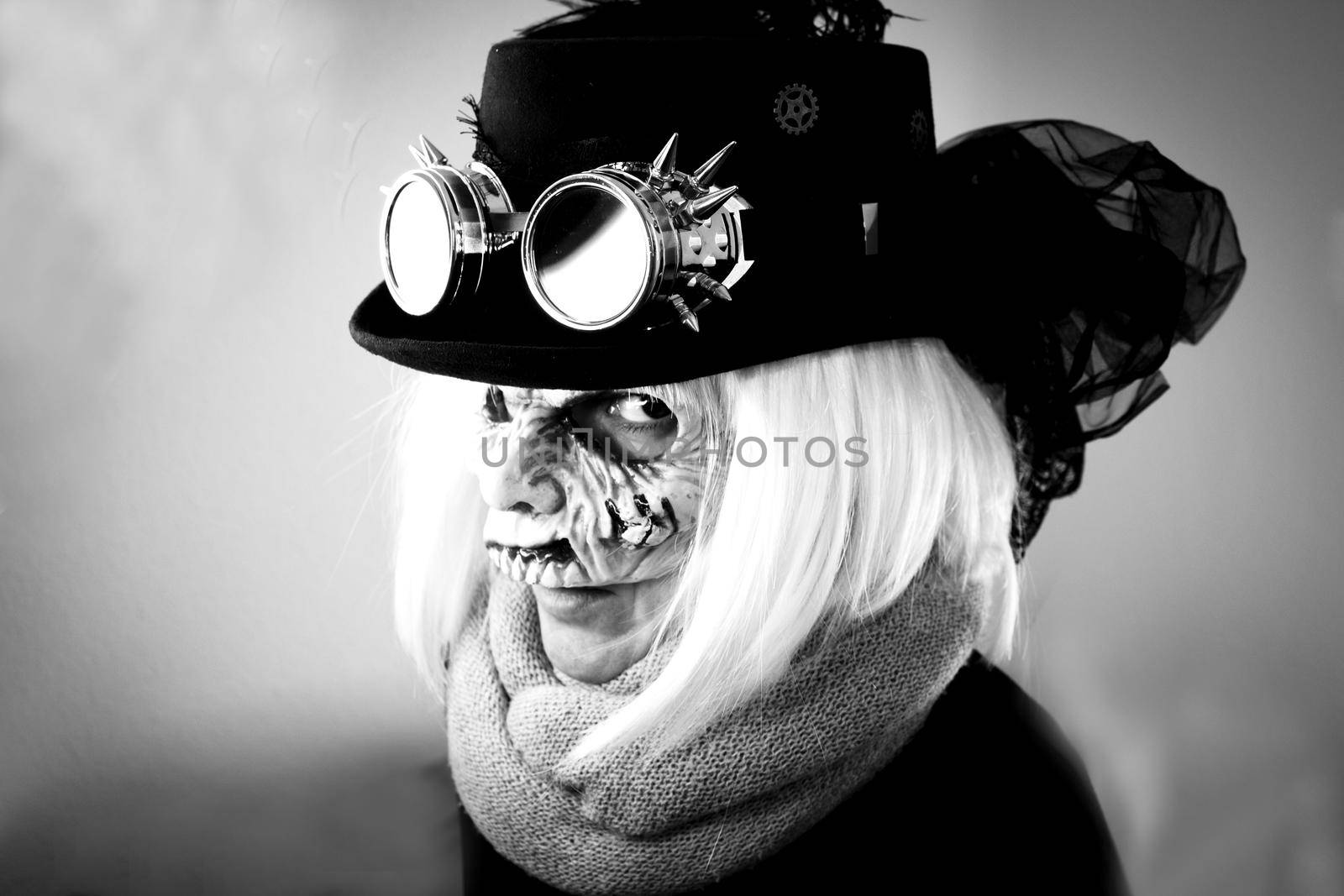 Woman with monster face and black hat wearing steampunk glasses. White hair.