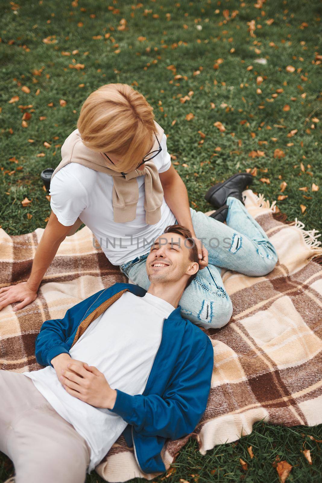 Loving gay couple having romantic date outdoors. Two handsome men sitting together on blanket in park. LGBT concept.