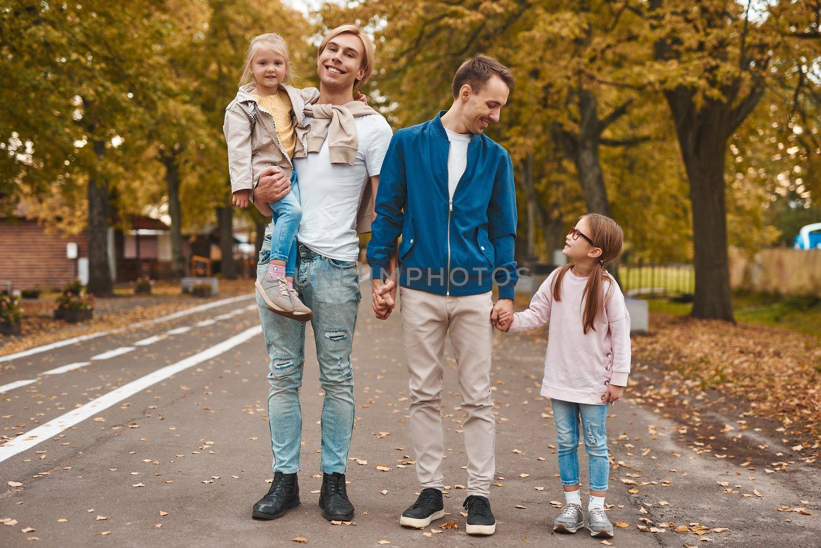 Two gay parents with their adopted daughters walking in park together. Happy LGBT family concept.