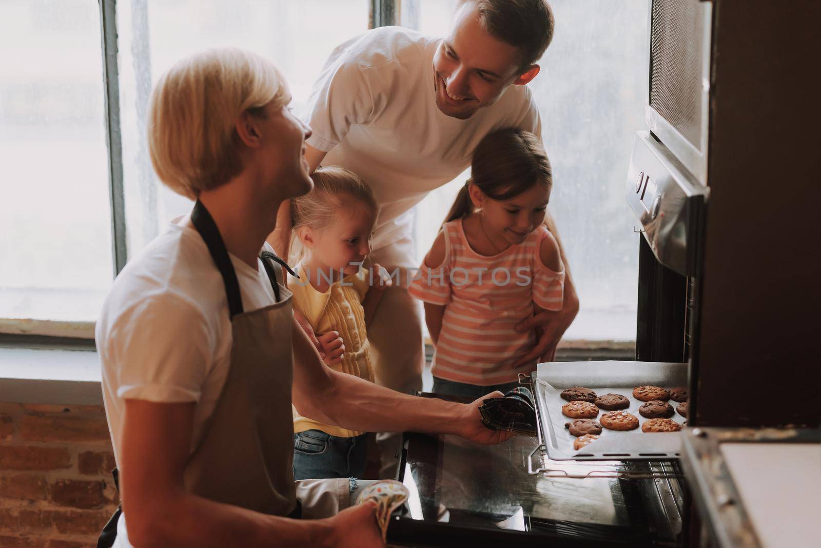 Gay couple with their adopted cute daughters cooking on kitchen. Lgbt family at home. Happy family making cookies together.