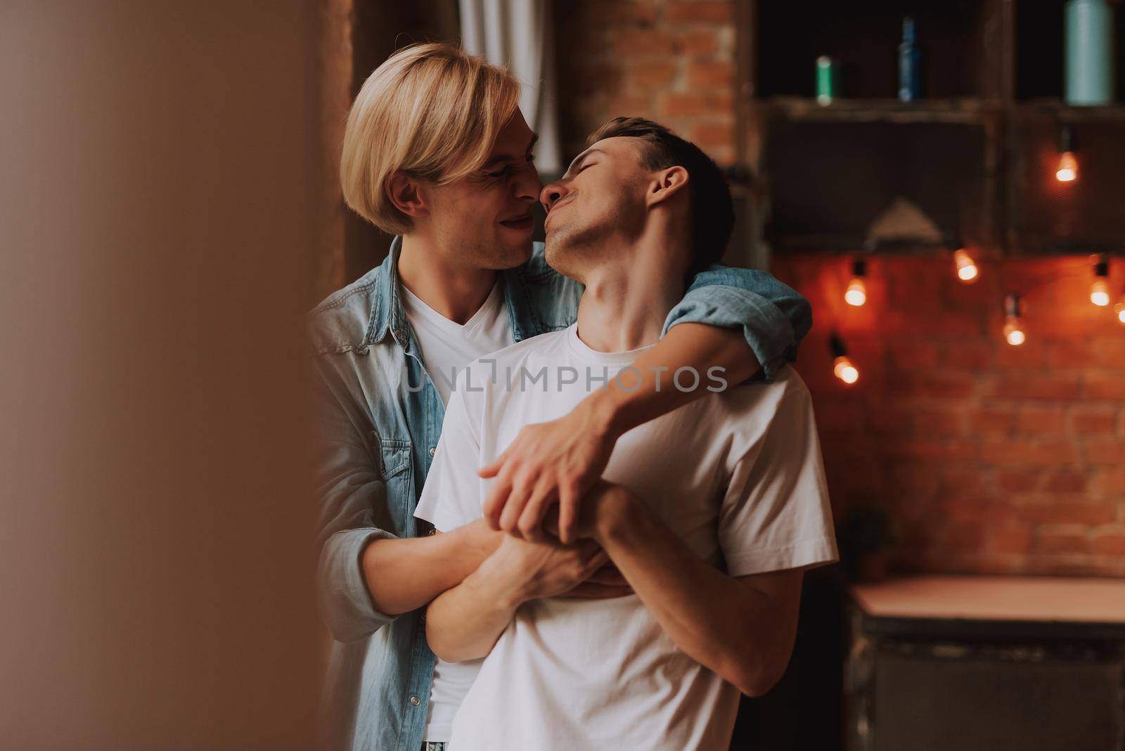 Loving gay couple at home. Two handsome men hugging and kissing on kitchen. LGBT concept.