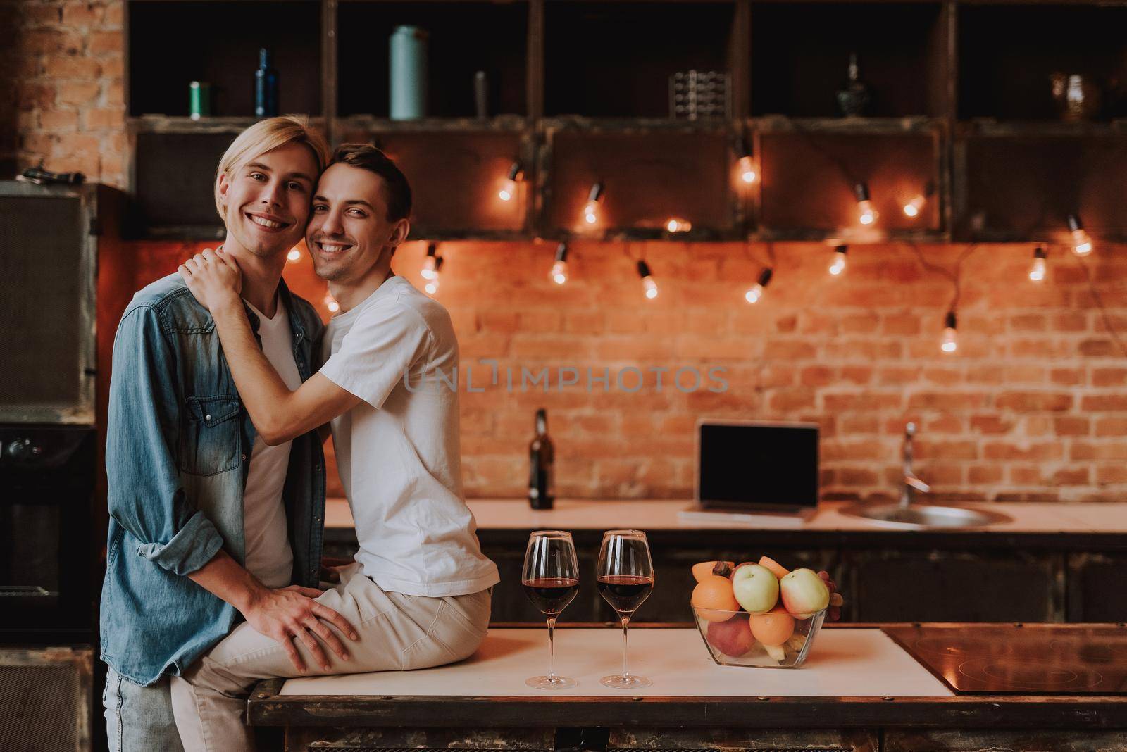 Loving gay couple at home. Two handsome men hugging and kissing on kitchen. LGBT concept.