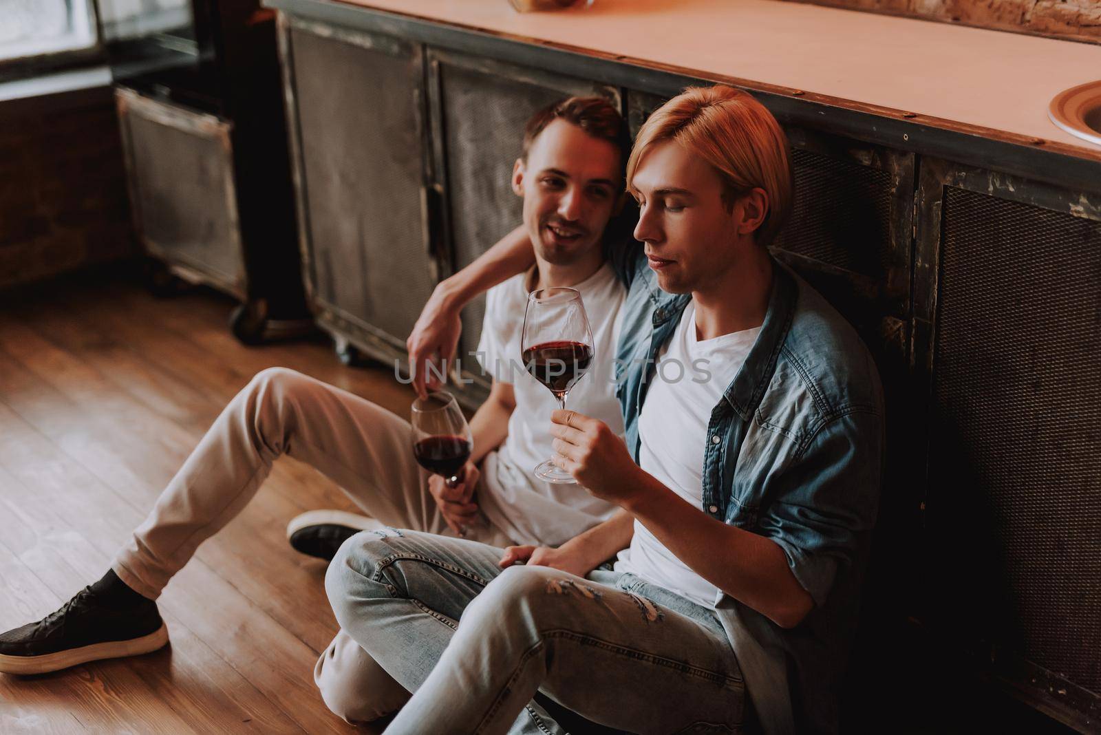 Loving gay couple at home. Two handsome men hugging, kissing and drinking wine on kitchen. LGBT concept.