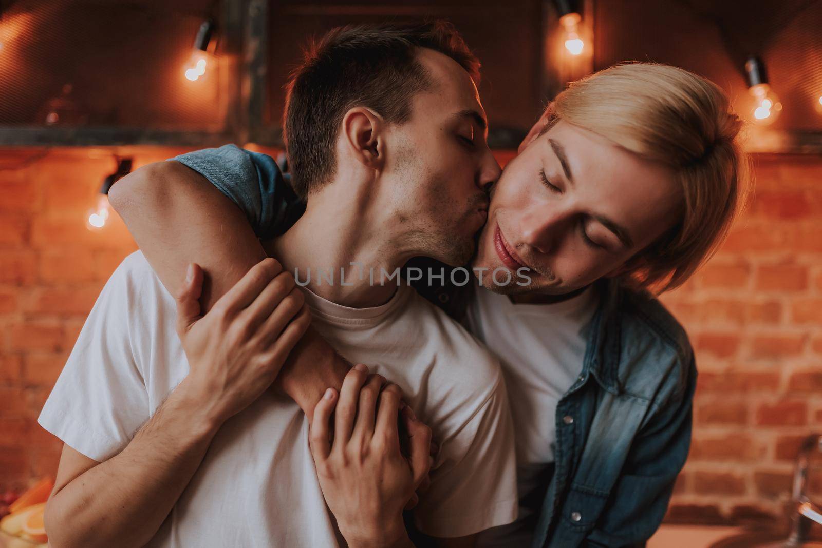 Loving gay couple at home. Two handsome men hugging and kissing on kitchen. LGBT concept.