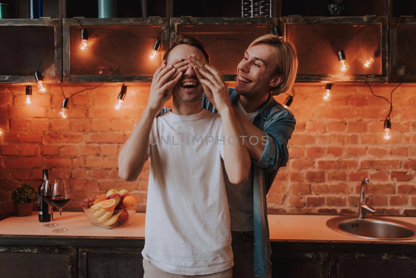 Loving gay couple at home. Two handsome men hugging and kissing on kitchen. LGBT concept.