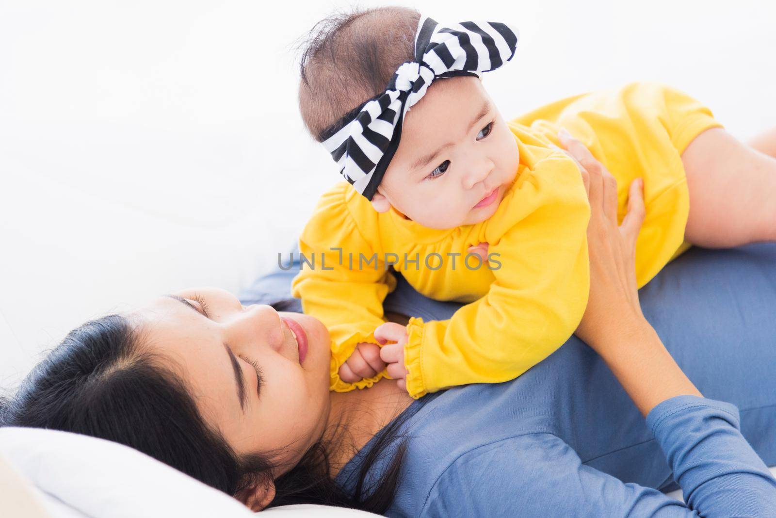 Portrait of beautiful young Asian mother playing and smiling together with his newborn little baby at home, Parent mom and little kid relaxing in the bedroom, Family having fun together