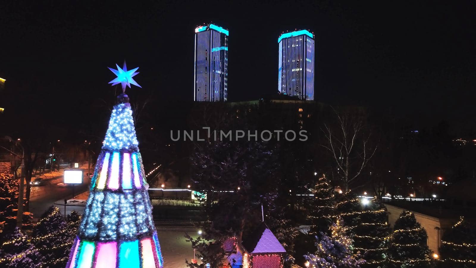 The city is decorated for Christmas and new year. Buildings, garlands, Christmas trees, fences and the square glow with different lights. People relax, enjoy the winter and holiday. View from a drone