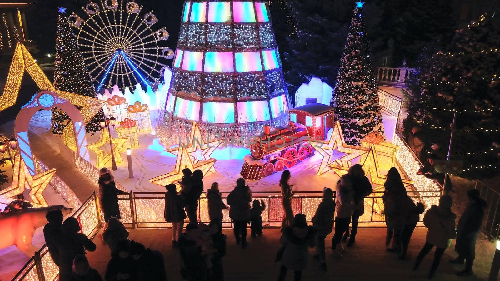 The city is decorated for Christmas and new year. Buildings, garlands, Christmas trees, fences and the square glow with different lights. People relax, enjoy the winter and holiday. View from a drone