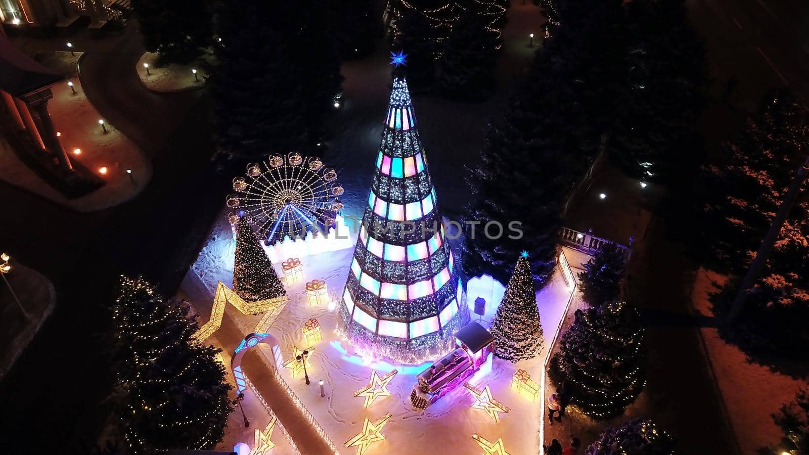 The city is decorated for Christmas and new year. Buildings, garlands, Christmas trees, fences and the square glow with different lights. People relax, enjoy the winter and holiday. View from a drone