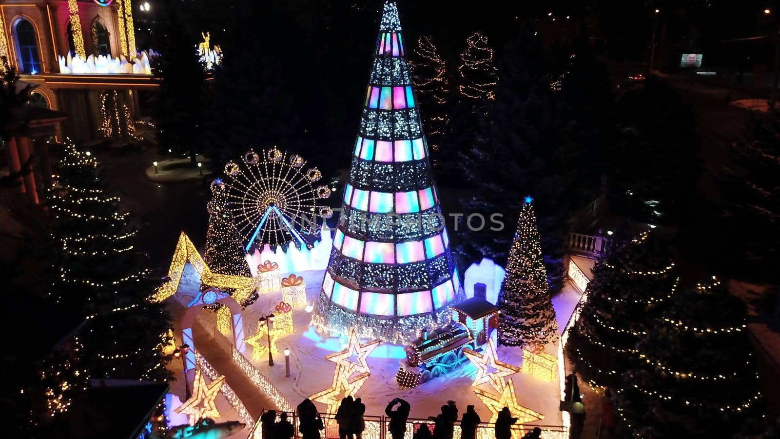 The city is decorated for Christmas and new year. Buildings, garlands, Christmas trees, fences and the square glow with different lights. People relax, enjoy the winter and holiday. View from a drone