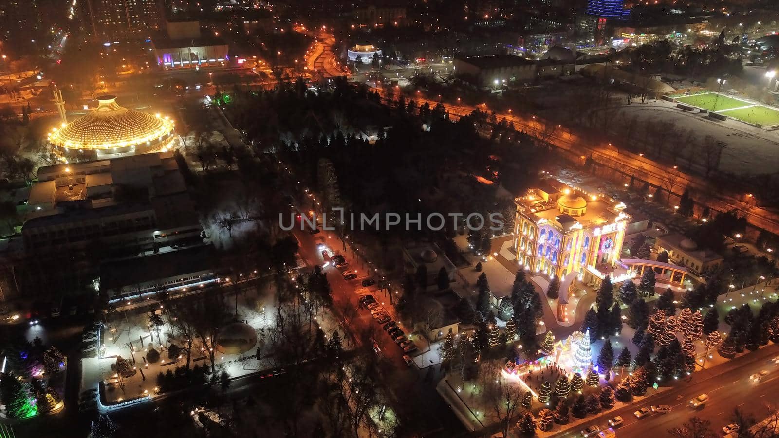 The city is decorated for Christmas and new year. Buildings, garlands, Christmas trees, fences and the square glow with different lights. People relax, enjoy the winter and holiday. View from a drone