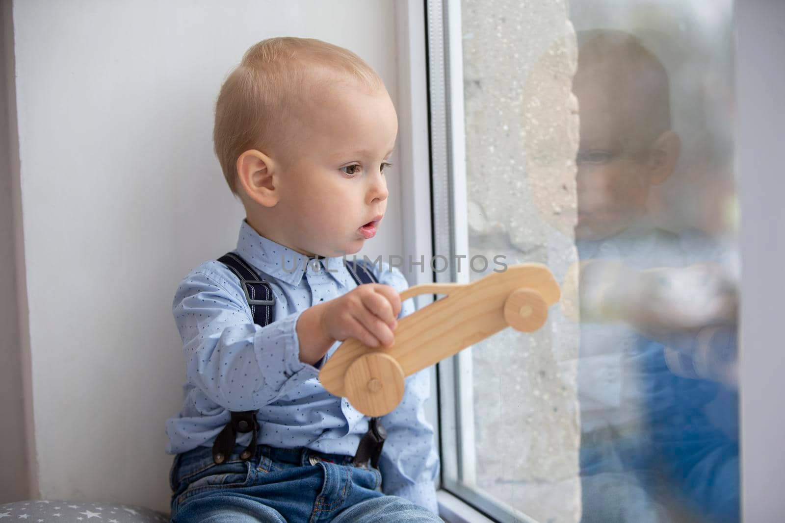 A small child looks out the window. The kid with a toy sits on a window sill.