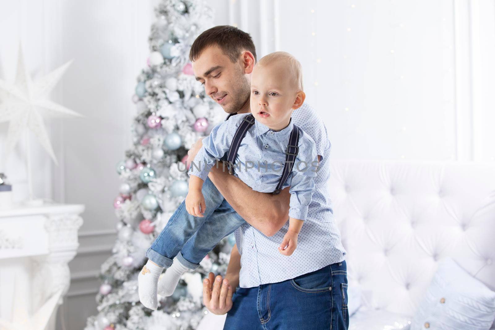 Father and child play against the background of a Christmas tree. Man and son in the new year. by Sviatlana