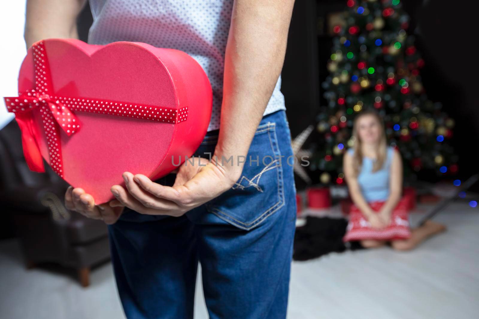 Hands holding a red gift box on a background of the Christmas tree. Christmas present to the family.