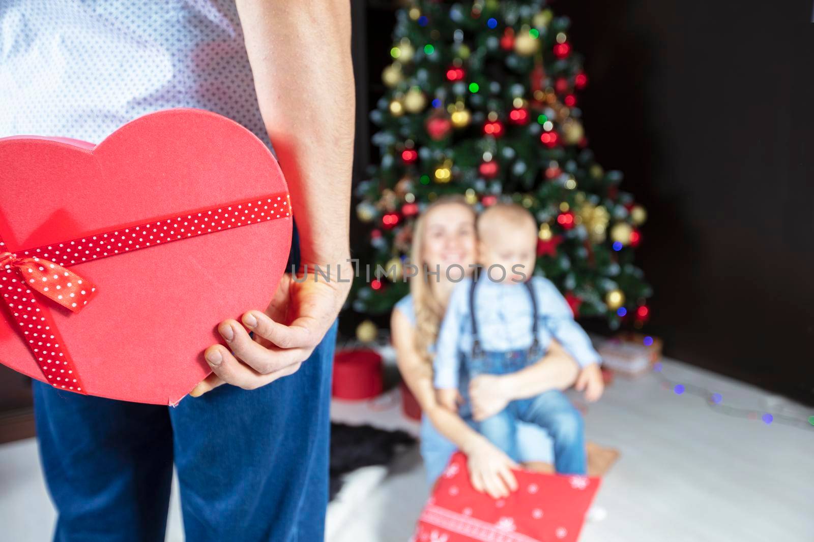 Hands holding a red gift box on a background of the Christmas tree. Christmas present to the family.