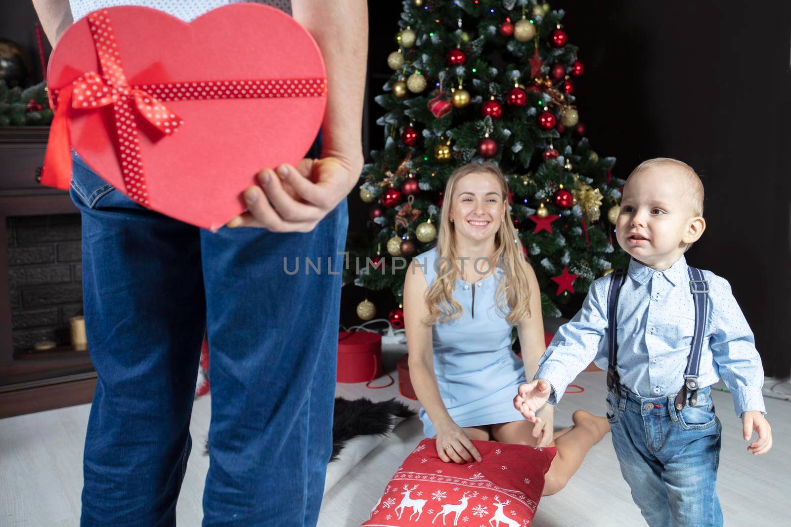 Christmas surprise. A man holds a red gift box on the background of his wife and child. Family on New Year's holidays. The little son runs to receive a Christmas gift.