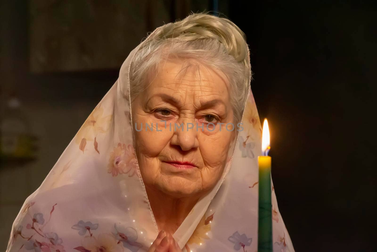 An elderly woman in a headscarf looks at a candle.An elderly woman is looking at a candle. The old woman is praying.