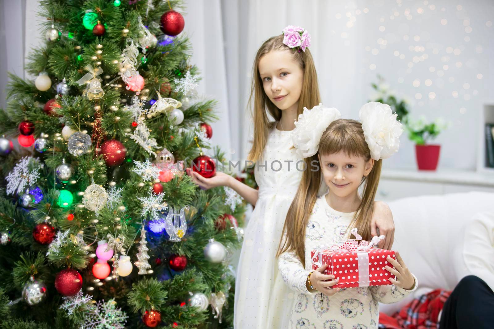 Two smart girls at the Christmas tree. Christmas holidays. New Year sisters at home.