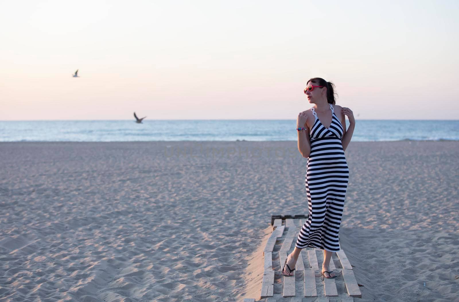 A woman in a striped dress stands on the seashore