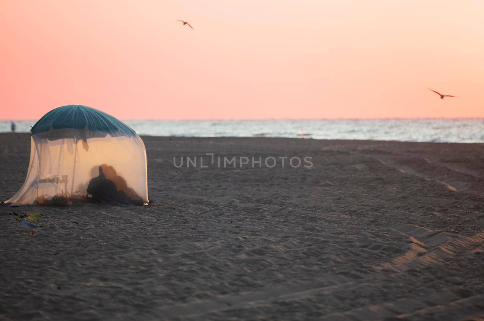 Relax on the beach in a tent. The coast and the silhouettes of people in the tent. by Sviatlana