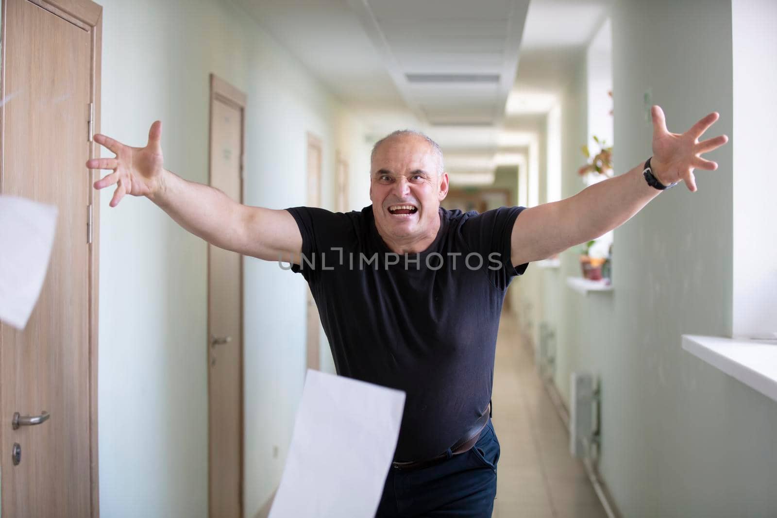 A man scatters sheets. Breakdown. Stress at work. An angry man in the hallway throws paper.