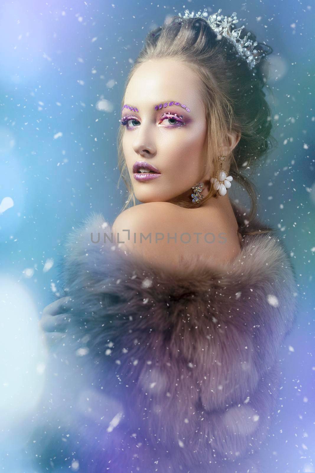 The Snow Queen. Winter girl in a fur coat showered with snow. Model with beautiful makeup on a snowy background.