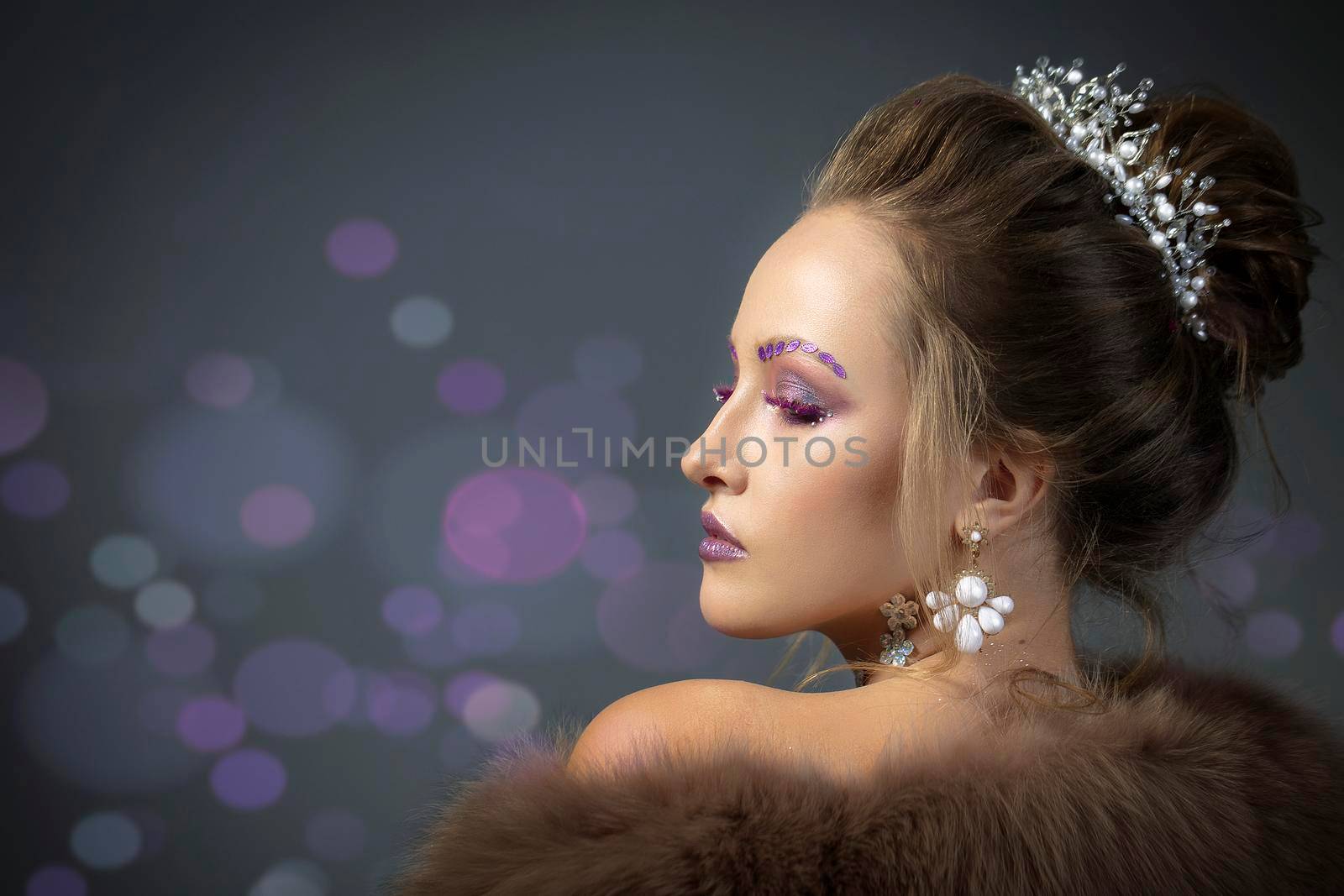 Beautiful model in profile with fashionable makeup in furs. Luxury winter girl on a gray background with bokeh.