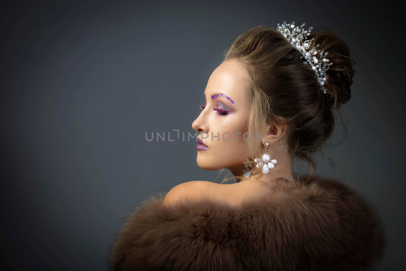 Beautiful model in profile with fashionable makeup in furs. Luxury winter girl on a gray background.