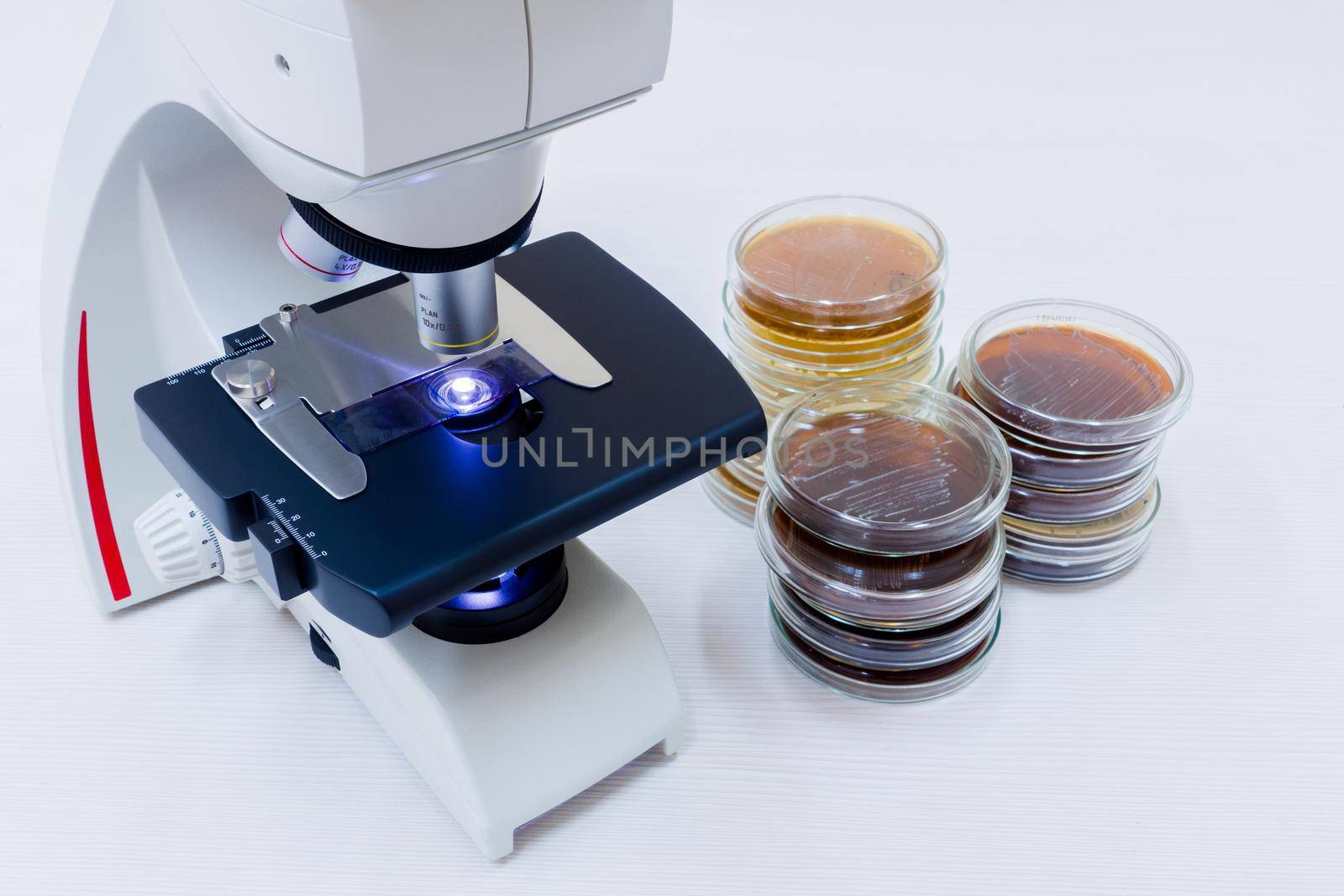 A microscope and petri dishes are near. A microscope on the desktop and next to it lie petri dishes.