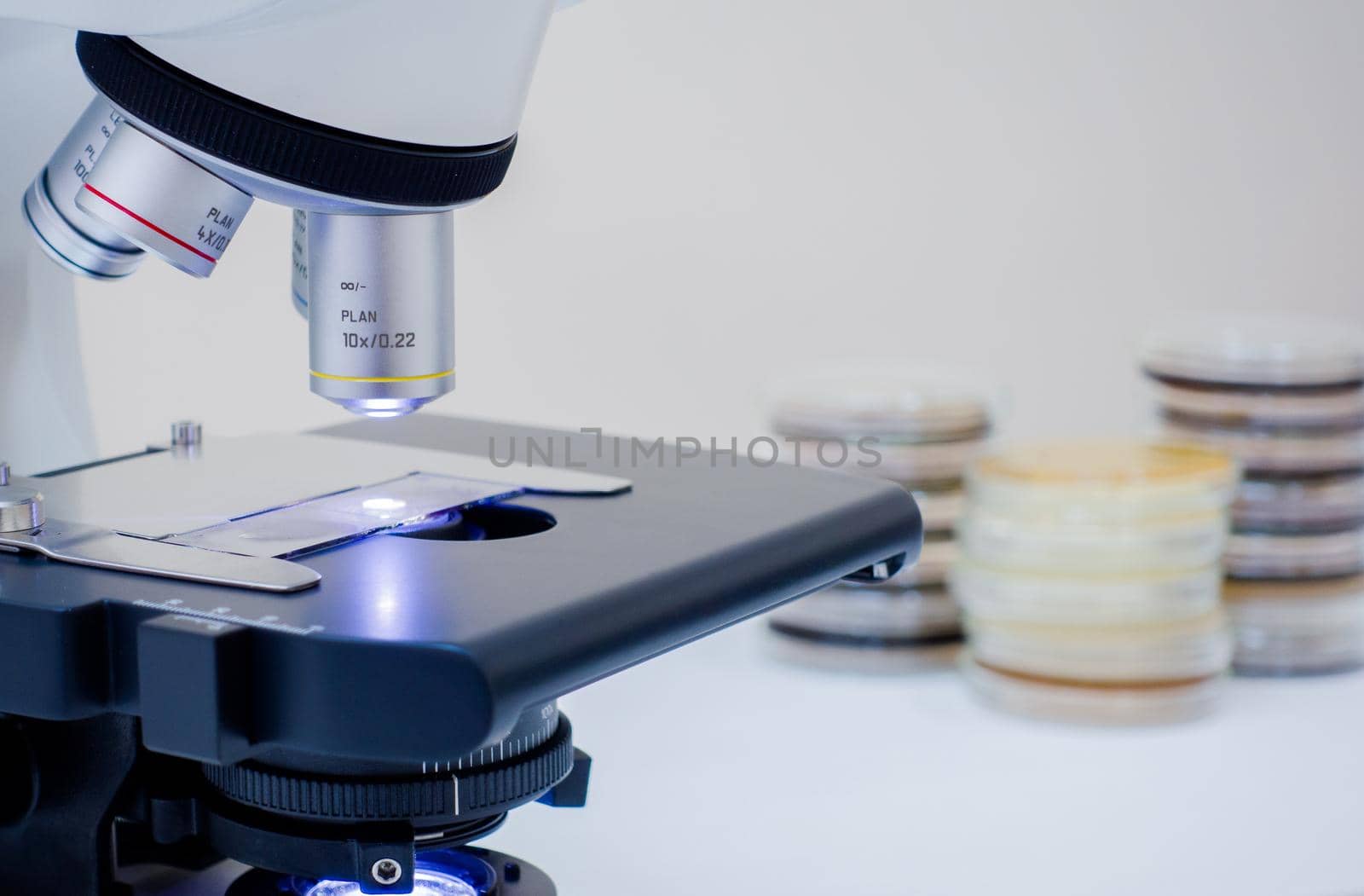 A microscope and petri dishes are near. A microscope on the desktop and next to it lie petri dishes. Glass on the microscope desktop.