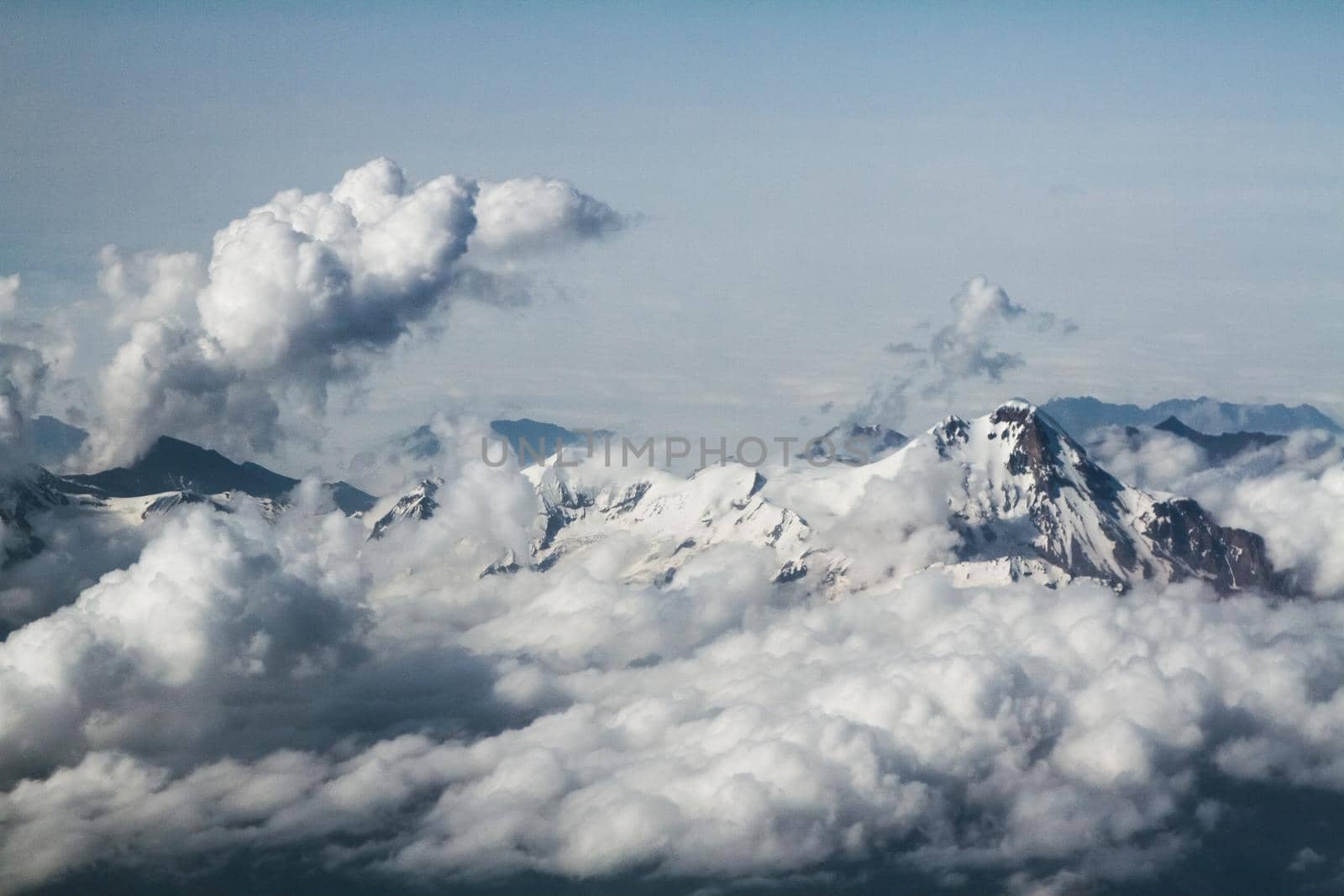 Mountain peaks in the clouds, top view, from the airplane. Clouds in the mountains.