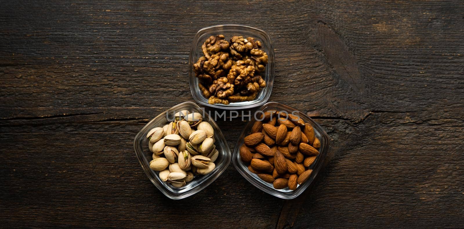Almond, pistachio and walnut in a small plates which standing on a vintage wooden table. Nuts is a healthy vegetarian protein and nutritious food