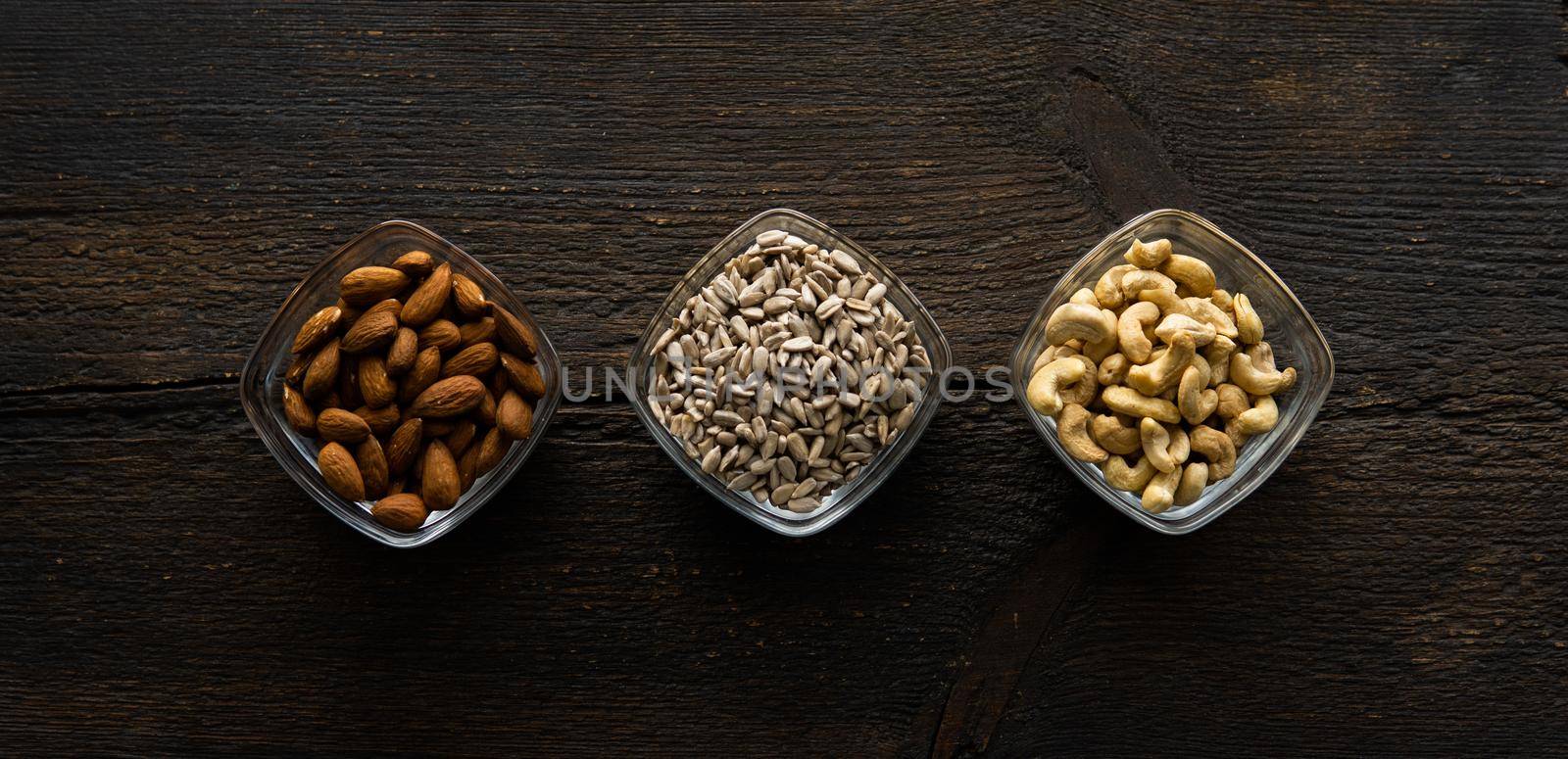 Almond, sunflower seeds and cashew in a small plates which standing on a vintage wooden table. Nuts is a healthy vegetarian protein and nutritious food. by vovsht