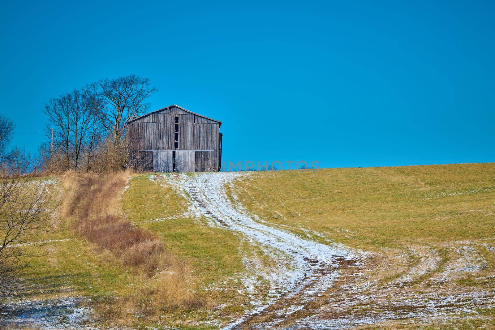 Tobacco barn sitting on a hill with snow covered path.