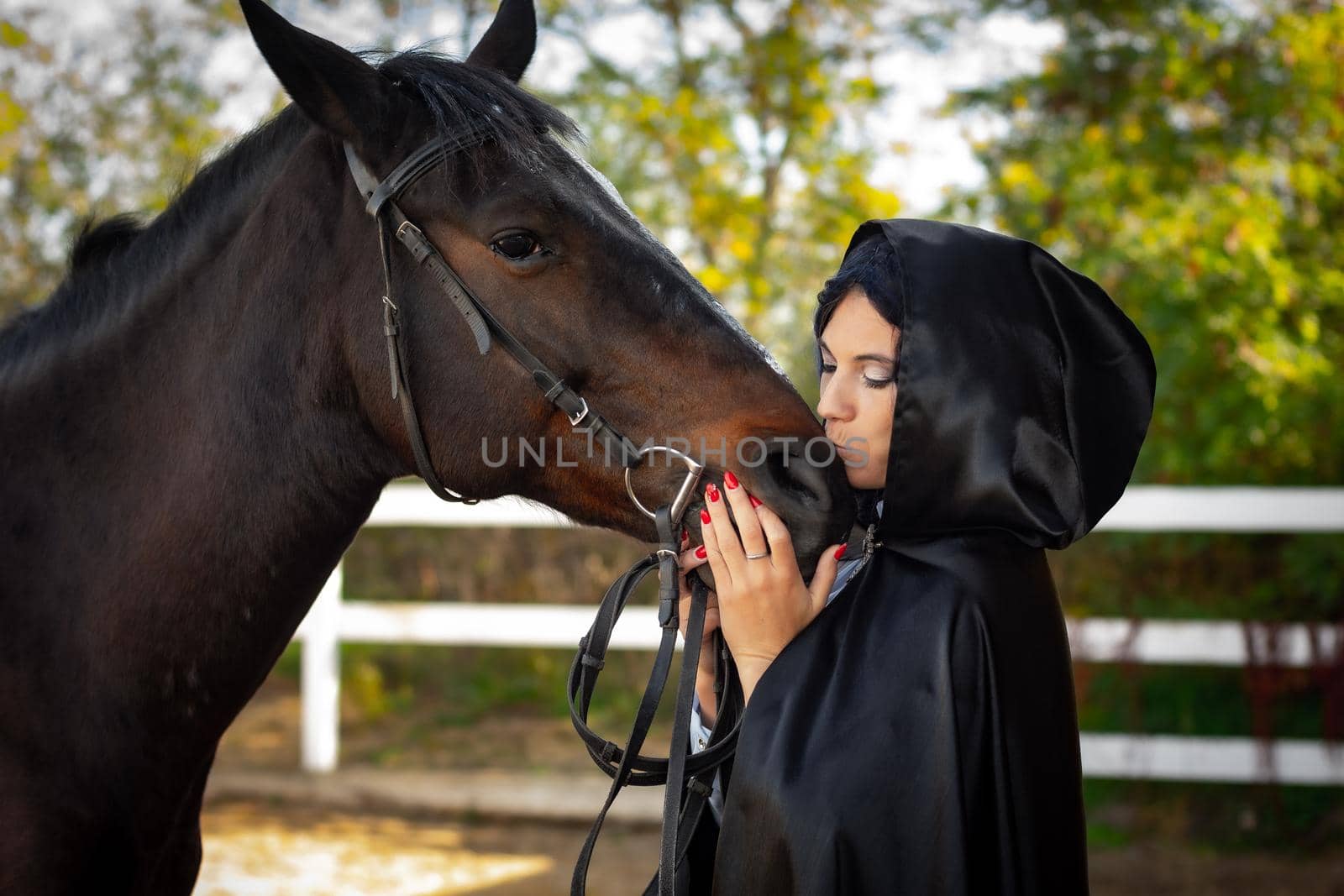Girl in a black cloak hugs and kisses a horse by Madhourse
