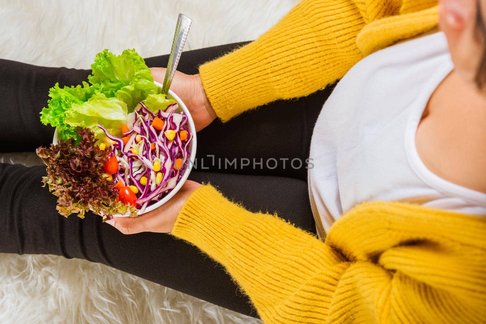 Top view of female hands holding bowl with green lettuce salad on legs, a young woman eating fresh salad meal vegetarian spinach in a bowl, Clean detox healthy food concept