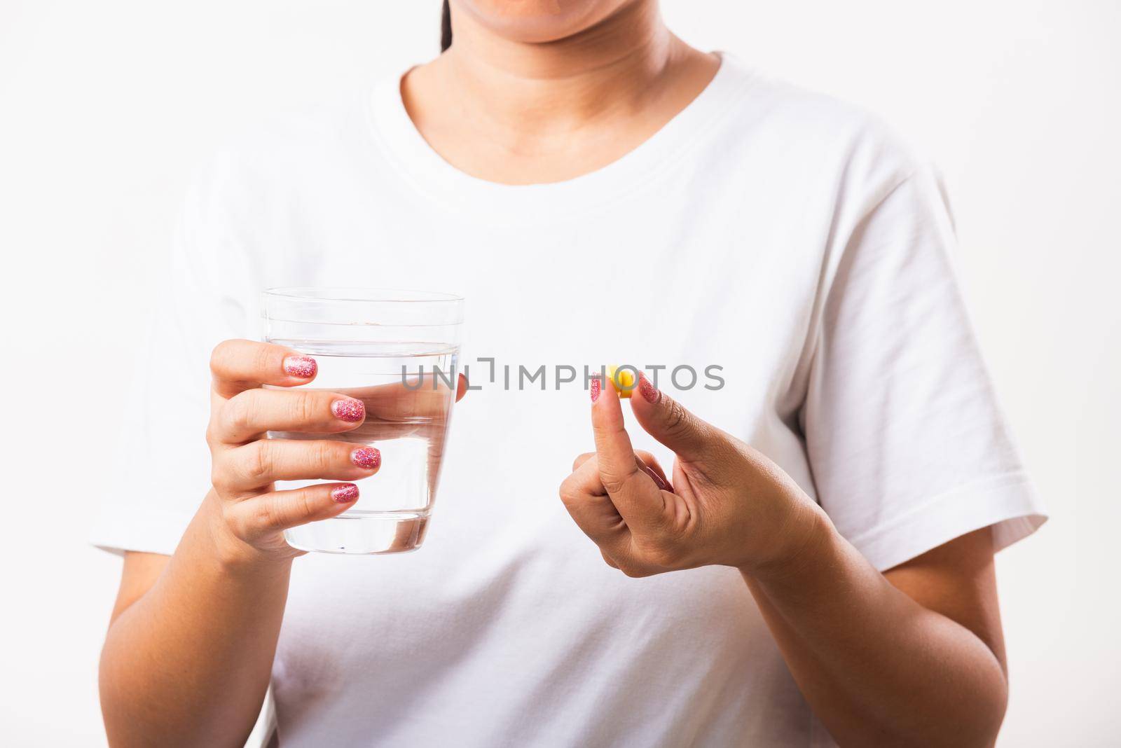 Closeup young Asian woman hold fish oil vitamin drugs in hand ready take medicines with a glass of water, studio shot isolated on white background, Healthcare and medical pharmacy concept