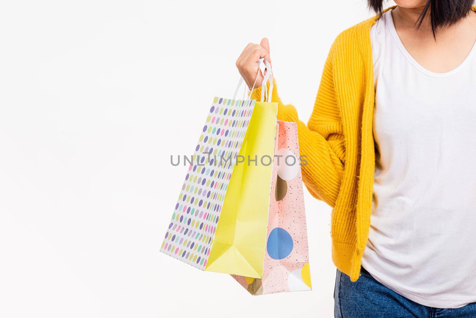 Happy young female hold many packets within arms, woman hand she wears a yellow shirt holding shopping bags multicolor isolated on white background, Black Friday sale concept