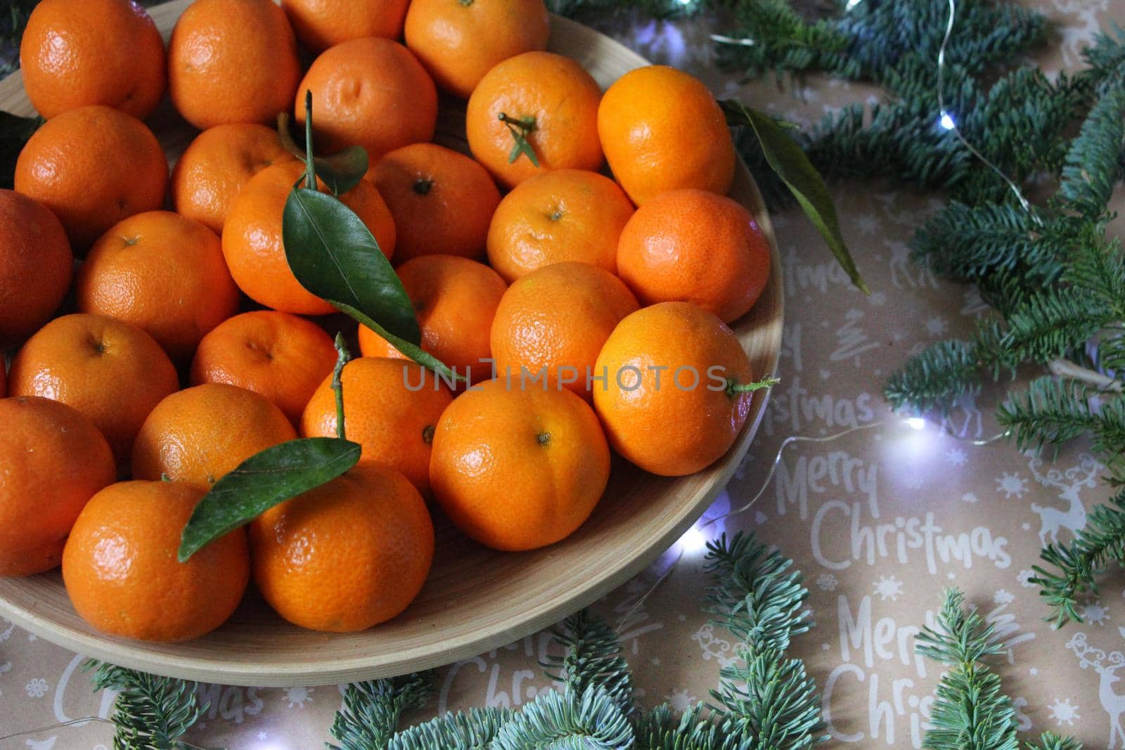 Small tangerines are laid out on a plate and decorated with a Christmas garland and coniferous green branches. Texture or background