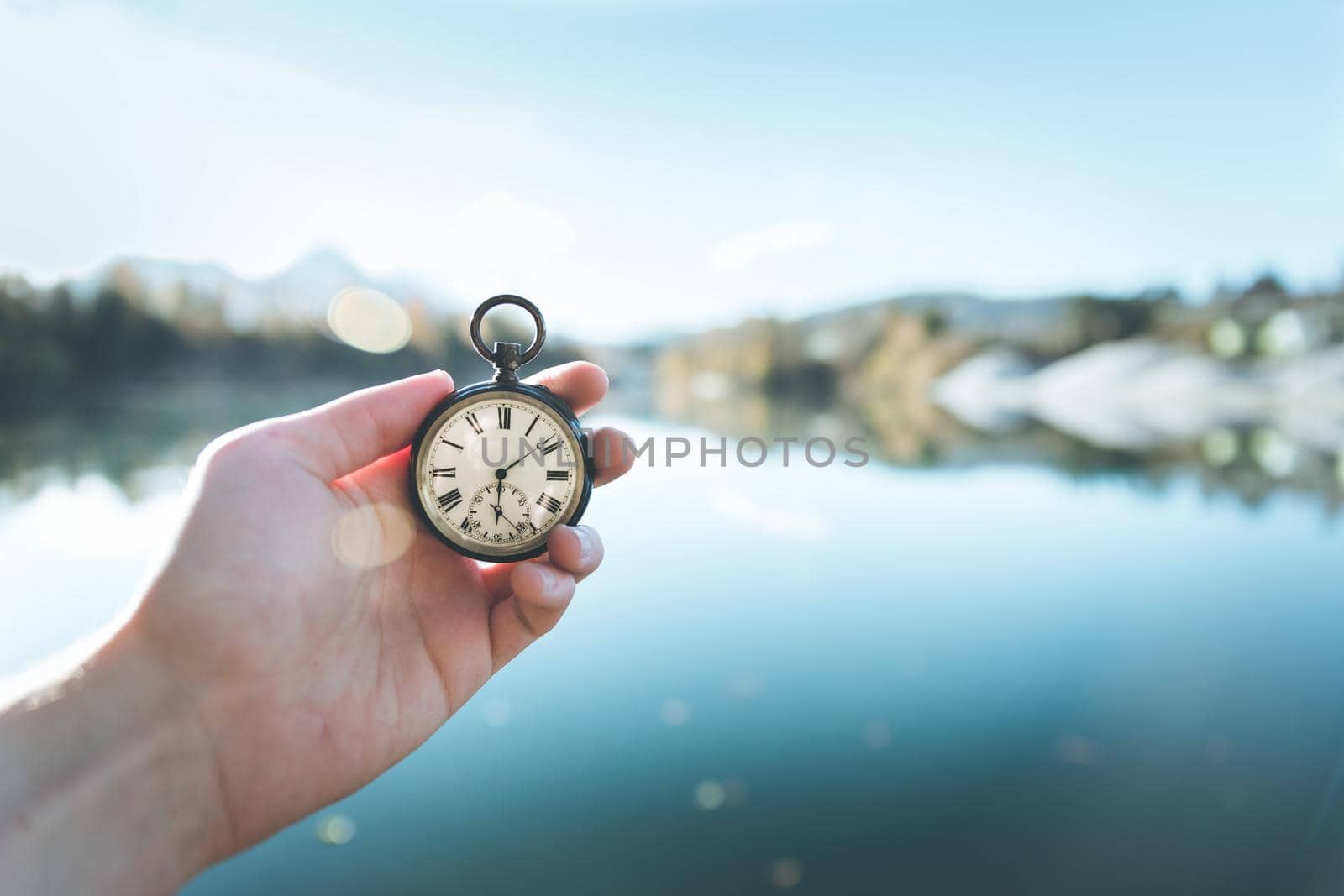 Hand held stop watch outdoors, autumn, blurry blue lake in the background