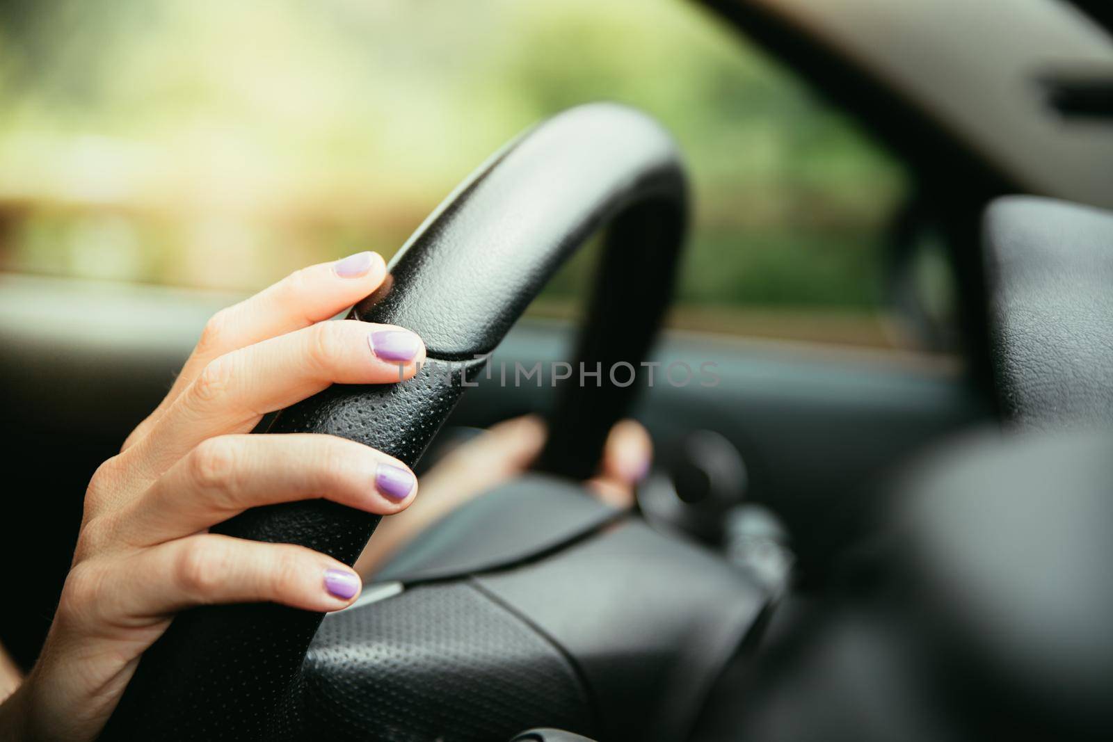 Sports car steering wheel, hands of a young girl with purple nail polish by Daxenbichler