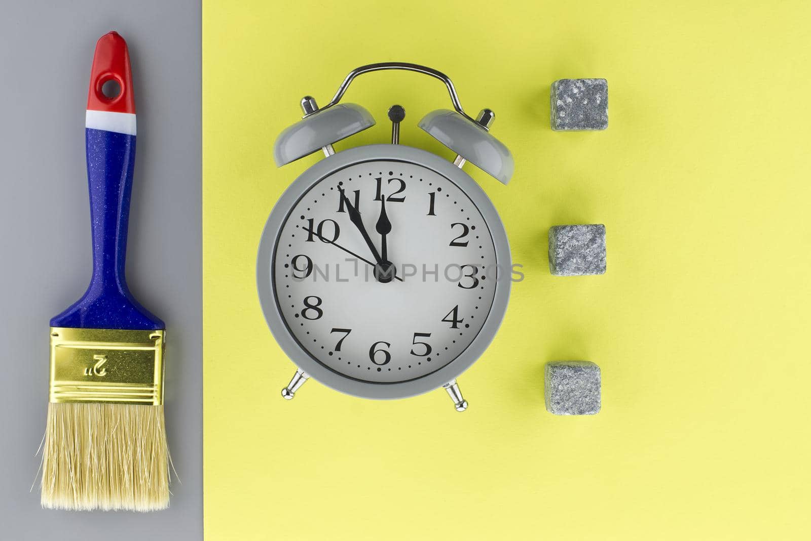 Conceptual image of alarm clock and new clean paintbrush on a two tone grey and yellow background with copyspace viewed as a flat lay still life