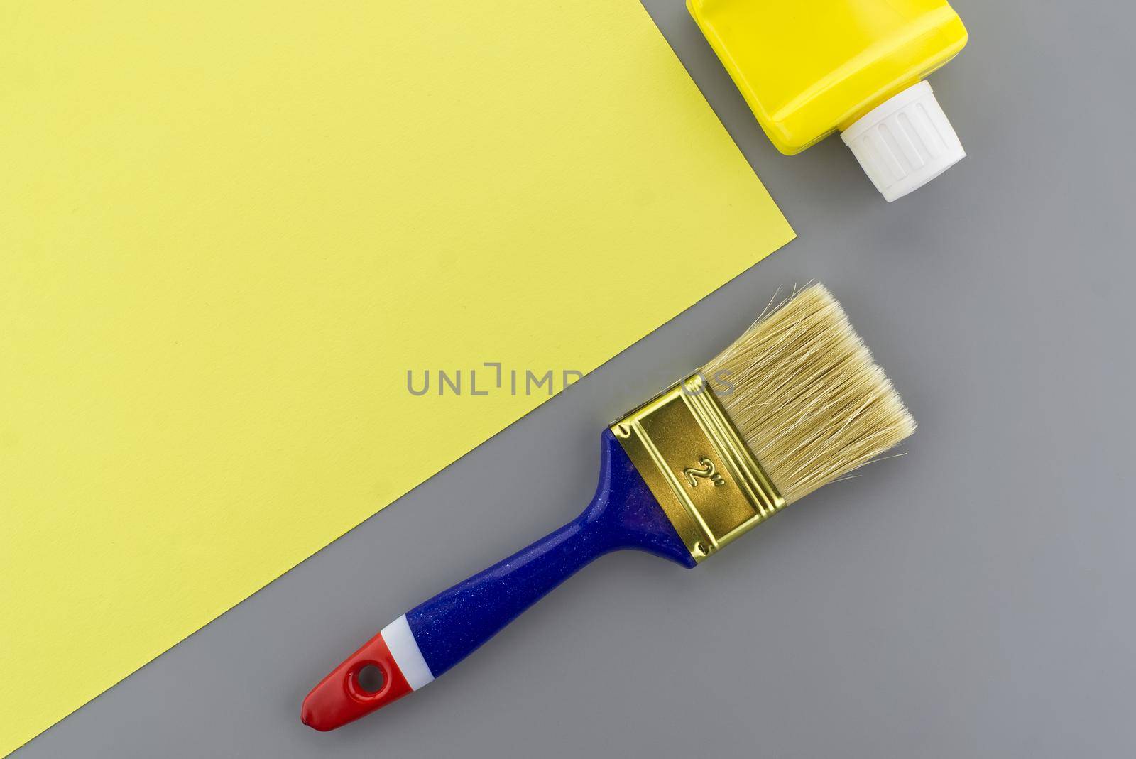 Renovation and color trends concept with clean paintbrush and pigment bottle on a two tone grey and yellow background with copy space viewed as a flat lay.